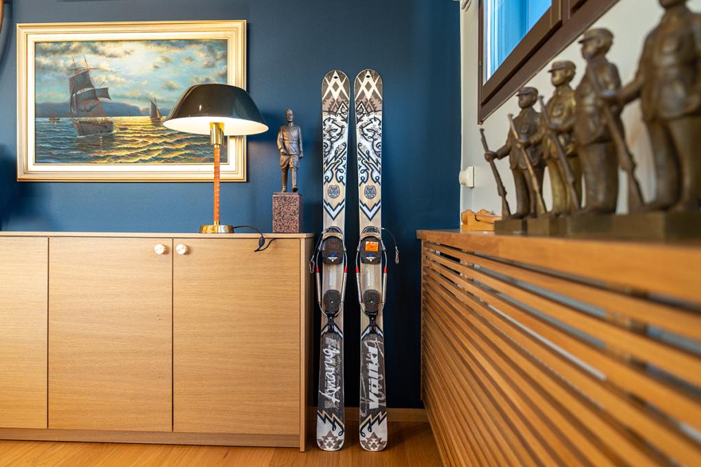 Telemark-sukset nojaavat seinään olohuoneessa, jossa on sininen seinä ja seinällä maisemataulu.