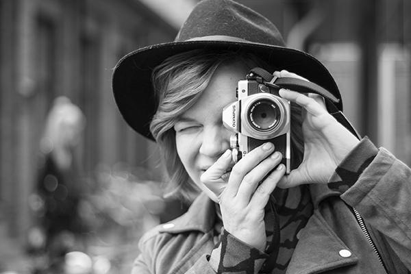 Mustavalkoinen kuva, jossa nainen katsoo kameraan toisen kameran linssin läpi.